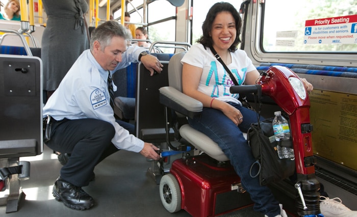 Happy woman on a mobility scooter being buckled into a bus by the bus driver